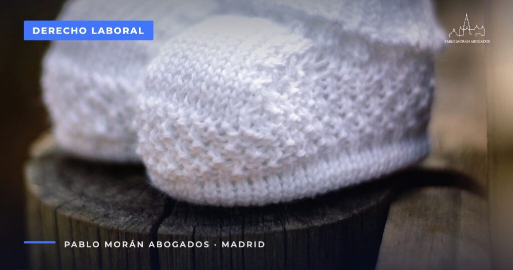 Patucos blancos de punto de bebé sobre madera rústica: despido de una trabajadora embarazada, abogado laboral en Madrid