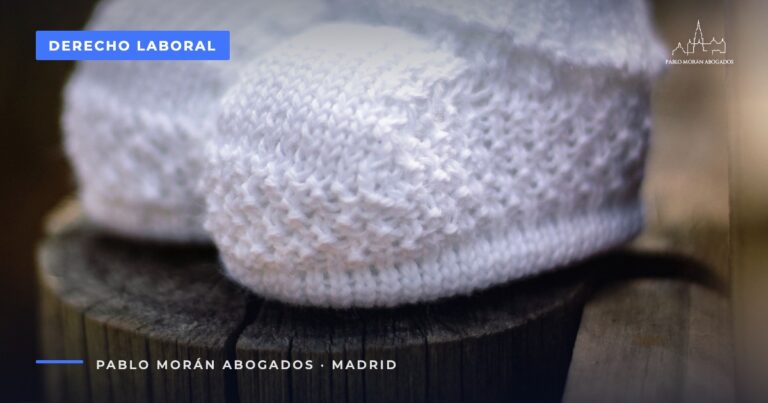 Patucos blancos de punto de bebé sobre madera rústica: despido de una trabajadora embarazada, abogado laboral en Madrid