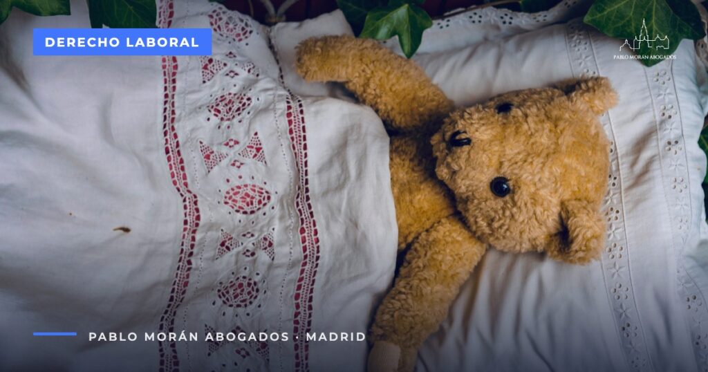 Osito de peluche sobre una cama con sábanas bordadas: cuidado de menores con cáncer o enfermedad grave, reducción de jornada, abogado laboral en Madrid