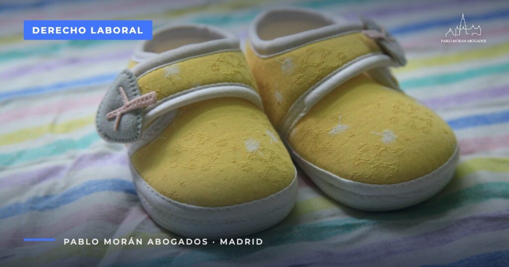 Zapatitos amarillos de bebé sobre una tela de rayas de colores: permiso de nacimiento de 19 semanas, abogado laboral en Madrid