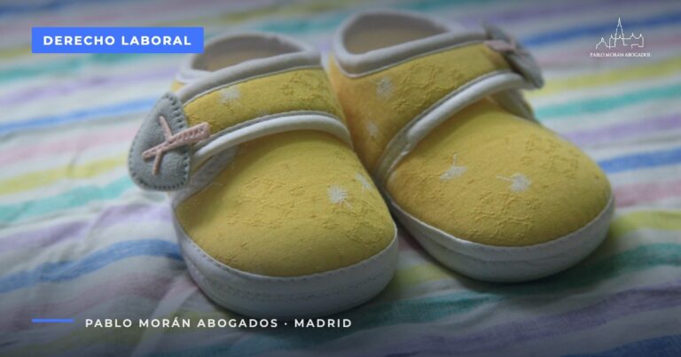 Zapatitos amarillos de bebé sobre una tela de rayas de colores: permiso de nacimiento de 19 semanas, abogado laboral en Madrid